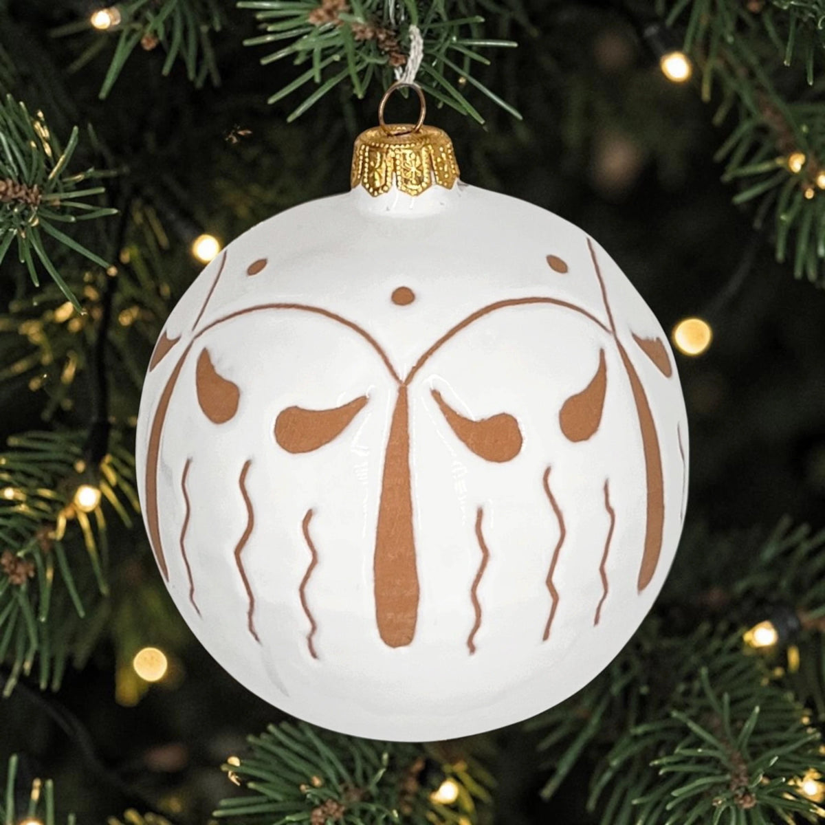 Palla di Natale artigianale in ceramica bianca con decori geometrici appesa tra i rami dell'albero illuminato