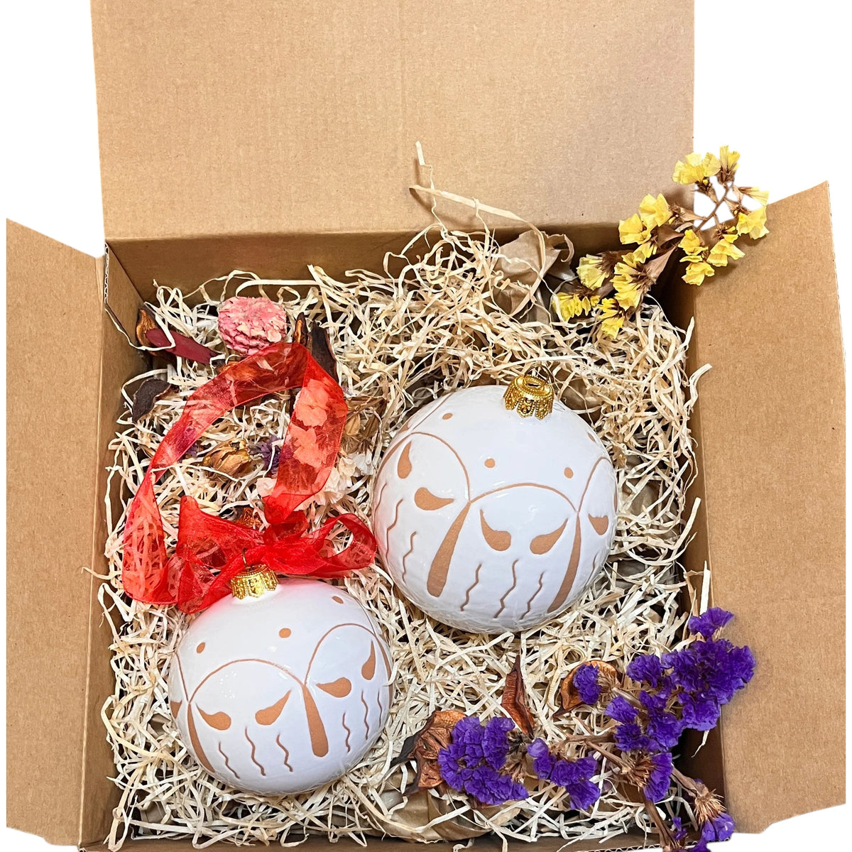 Set di sfere natalizie artigianali in ceramica bianca con decori geometrici, disposte in una scatola regalo con trucioli e dettagli floreali.